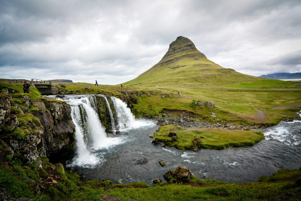 Veduta del monte Kirkjufell a forma di cono e delle cascate Kirkjufellsfoss che si gettano in un fiume in Islanda